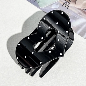 Close-up of heart-shaped black hair claw clip with white polka dots on leather background
