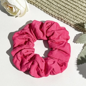 Detailed close-up of a magenta ribbed knit scrunchie on a white textured leather surface
