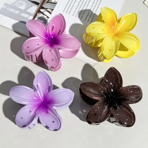 Detailed close-up of four colorful gradient plumeria hair claws on a textured background