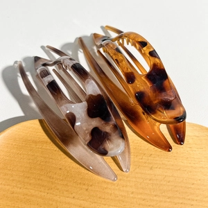 Close-up of leopard print and marble hair clips on a light wood tray in soft light
