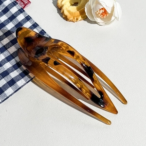 Close-up of tortoise shell leopard hair claw clip on aesthetic white leather background