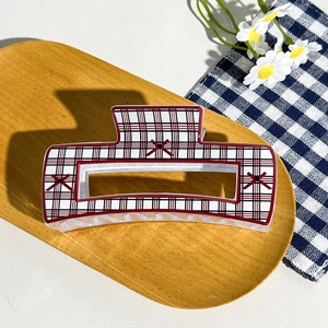 Detail view of large checkered hair claw clip with red X patterns on a wooden tray
