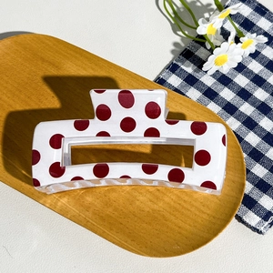 Detail view of a white checkered hair claw clip with red dots on a wooden tray