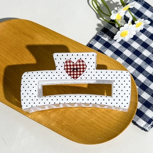 Close-up of white hair claw clip with black polka dots and red checkered heart detail