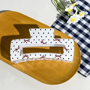 Detail shot of a checkerboard hair claw clip with red bow pattern on a wooden tray
