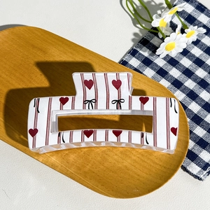 Detail of checkered hair claw with red stripes and heart patterns on a wooden tray