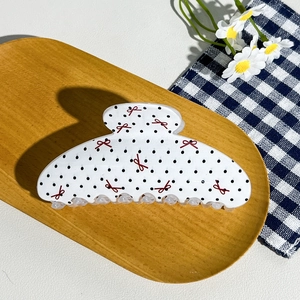 Close-up of a cream hair claw clip with black polka dots and small red bows on a tray