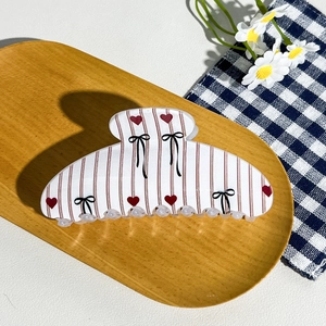 Detail of checkered hair claw clip with red hearts and black bow on wooden tray
