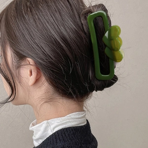 Green rectangular hair claw clip with heart accents on model's sleek updo hairstyle