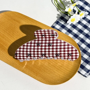 Macro shot of large red and white checkered hair claw clip with black bows on a wooden tray