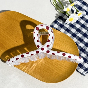 Detail view of large checkered hair claw clip with red dots on a wooden background