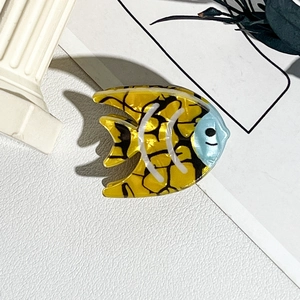 Détail d'une pince à cheveux poisson jaune et bleu sur fond blanc texturé