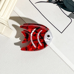 Détail d'une pince à cheveux carpe koï rouge en acétate brillant sur un fond décoratif