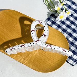 Detail of checkered hair claw clip with black dots and red bows on a wooden tray