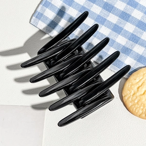 Close-up of gloss black hair claw clip with interlocking teeth on white textured background