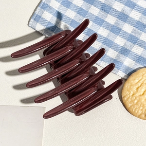 Close-up of a burgundy hair claw clip with cross teeth on a minimalist textured surface