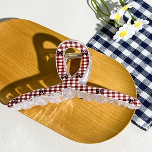 Detail of red checkered hair claw clip with bow pattern on wooden tray and daisy background
