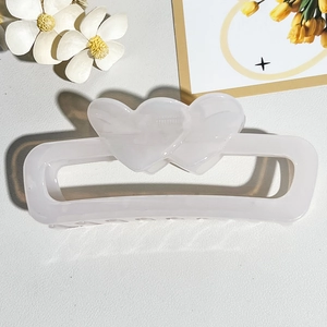 Detail view of translucent white heart-shaped rectangular hair claw on leather background