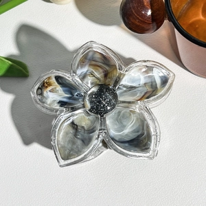 Macro detail of frangipani hair claw with marble texture and black glitter center