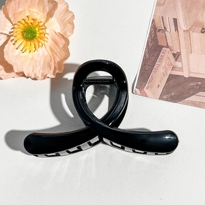 Detail view of glossy black twisted hair claw clip on elegant white leather background