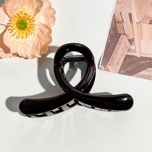 Detail of elegant black glossy hair claw clip with twisted ribbon design on leather surface