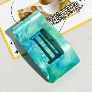 Detail of teal marble acetate hair claw clip with rectangular cutout on marble surface