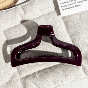 Top view of a deep purple glossy fishtail hair claw clip on beige linen fabric
