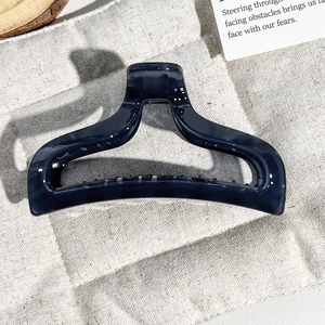 Detail of large navy blue marble hair claw clip with geometric hollow design on soft fabric