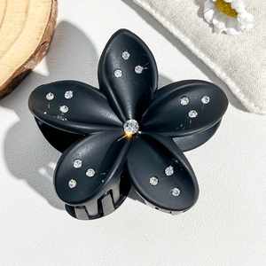 Detail of matte black 8cm frangipani hair claw clip with inlaid sparkling rhinestones