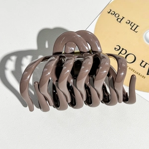 Detail of mocha brown resin hair claw clip with golden metal spring and wavy tooth design