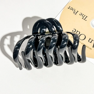Close-up of a large black glossy hair claw clip with a strong gold metal spring