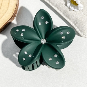 Detail view of a 8cm dark green flower hair claw clip with rhinestones on a wooden base