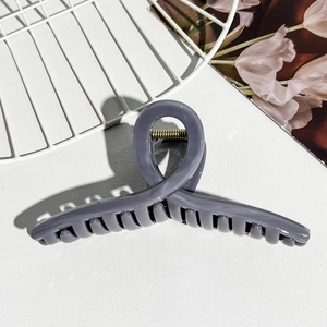 Detail of grey jelly hair claw clip with golden metal spring on white textured surface