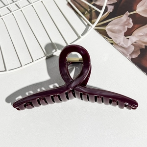 Detail shot of a dark burgundy jelly PC hair claw clip with golden spring on white texture
