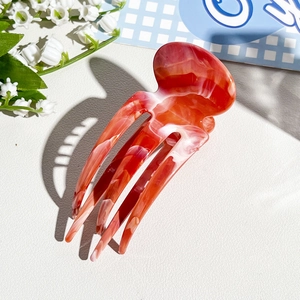 Detailed view of red marble hair claw clip with floral accents on white background