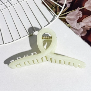 Detailed close-up of cream cross claw clip with golden metal spring on textured background