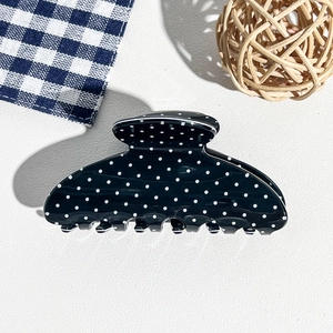 Detailed top view of a black hair claw with white polka dots on a textured background