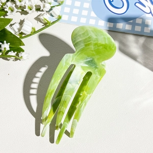 Detailed view of light green marble textured hair claw on white leather background