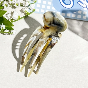 Detail view of the marble-textured resin four-prong hair clip on white leather
