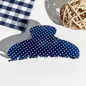 Close-up of a large navy blue hair claw clip with white polka dots on textured leather
