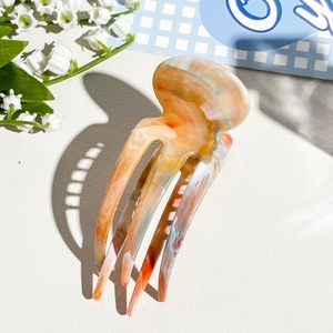 Detailed macro view of jellyfish-shaped hair claw with orange and blue marble resin texture