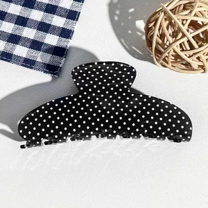 Close-up of vintage black hair claw clip with white polka dots on textured background