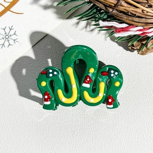 Detail of a wavy dark green Christmas hair claw with festive tree and hat decorations