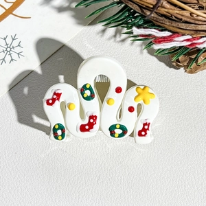 Detailed view of large white Christmas hair claw clip with festive sock and wreath patterns