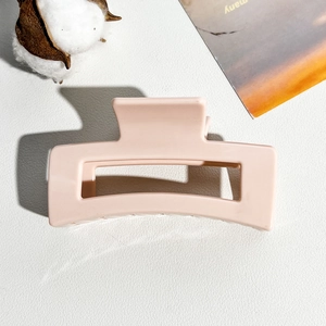 Detail of an 8.5cm square hollow hair claw clip in soft flesh pink on a textured surface