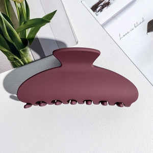 Close-up of a matte burgundy semicircular hair claw clip on a white leather surface