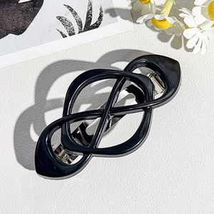 Detail of a black geometric knot hair clip with a silver metal spring clasp