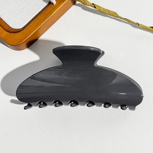 Detail showing high-gloss dark grey semi-circular hair claw clip on a textured background