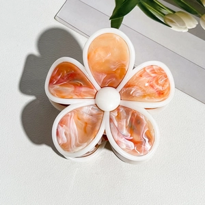 Detaillierte Makroaufnahme einer cremefarbenen Blumen-Haarklammer mit orangefarbenem Marmormuster