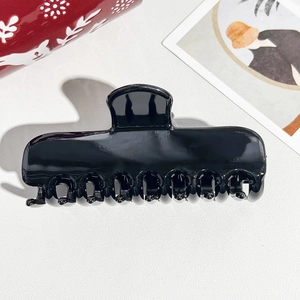 Top view of a glossy black medium hair claw clip with 10 teeth on white leather texture